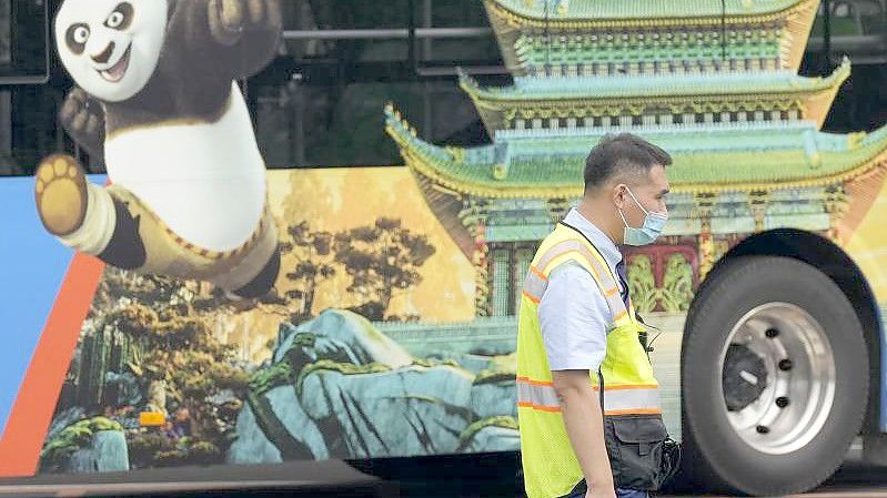 Ein Verkehrspolizist steht bei Probefahrten neben einem Bus, auf dem für den Vergnügungspark von Universal Studios geworben wird. Foto: Ng Han Guan/AP/dpa