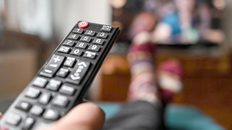 Ein junger Mann sitzt mit einer Fernbedienung vor dem Fernseher. Streaminggeräte in Deutschland bekommen von US-Riese Roku Konkurrenz. Foto: Britta Pedersen/dpa-Zentralbild/dpa