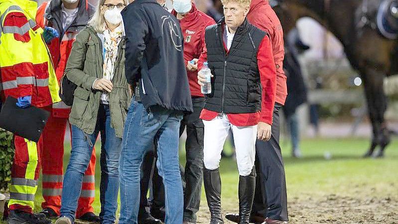 Marcus Ehning (2.v.r) steht nach seinem Sturz neben Sanitätern und Ärzten und Bundestrainer Otto Becker (r). Foto: Rolf Vennenbernd/dpa