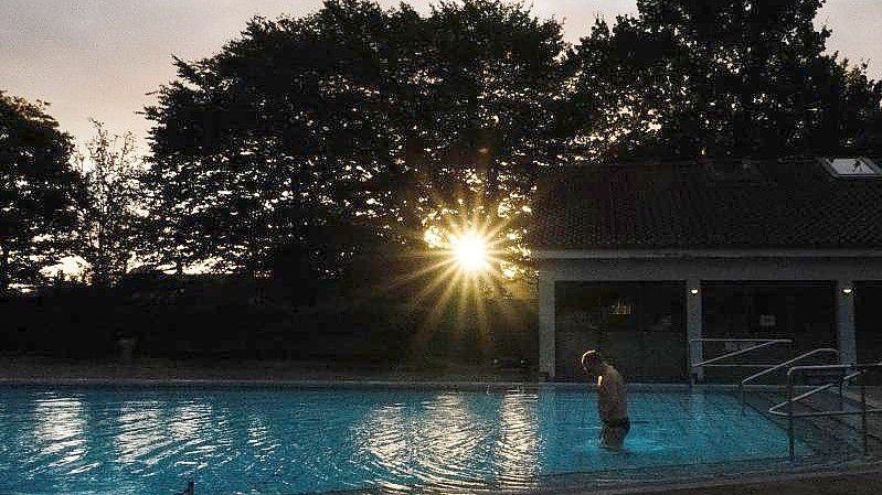 Ein Badegast steigt am frühen Morgen bei Sonnenaufgang ins Schwimmbecken im Freibad Großburgwedel bei Hannover. Foto: Demy Becker/dpa