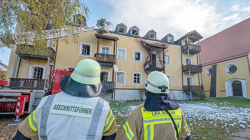 Feuerwehrmänner stehen vor einem ausgebrannten Mehrfamilienhaus. Foto: Armin Weigel/dpa