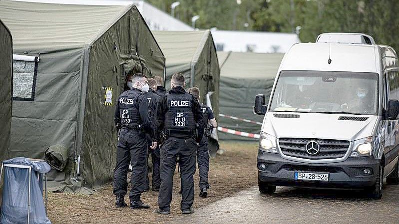 Polizisten in der Erstaufnahmeeinrichtung Eisenhüttenstadt neben einem Zelt für neu ankommende Asylsuchende. Foto: Fabian Sommer/dpa