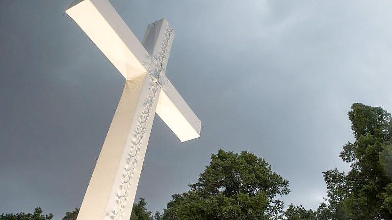 Dunkle Wolken über einem Kreuz. Foto: picture alliance / Lino Mirgeler/dpa