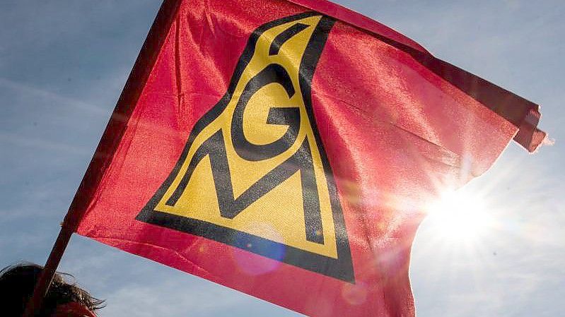 Teilnehmer einer Kundgebung halten eine Fahne mit dem Logo der IGM hoch. Foto: Daniel Bockwoldt/dpa/Daniel Bockwoldt