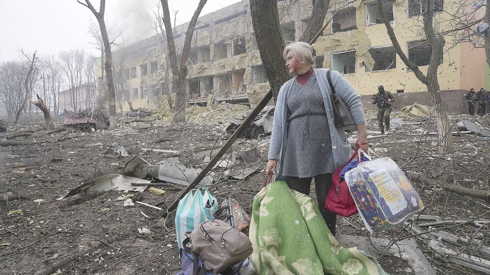 Eine Frau steht mit ihrem Gepäck vor einer durch einen Angriff beschädigten Geburtsklinik in Mariupol. Foto: DPA