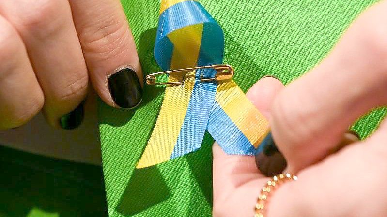 Ein Gast steckt sich aus Solidarität eine Schleife mit der ukrainischen Flagge an. Foto: Jens Kalaene/dpa-Zentralbild/dpa