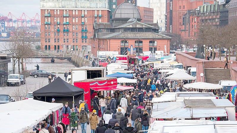 Besucher gehen am Morgen über den Hamburger Fischmarkt an der Elbe. er ist am Sonntag wieder in vollem Umfang gestartet. Foto: Daniel Bockwoldt/dpa