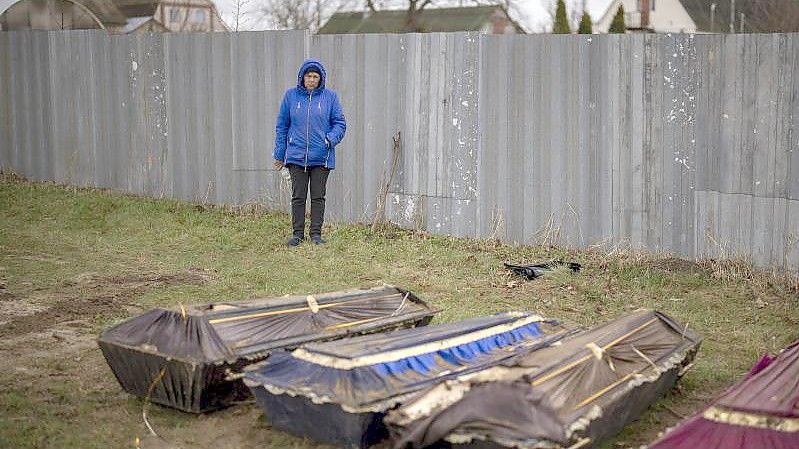 Eine Frau steht während der Exhumierung eines Massengrabes neben Särgen in Butscha. Foto: Emilio Morenatti/AP/dpa