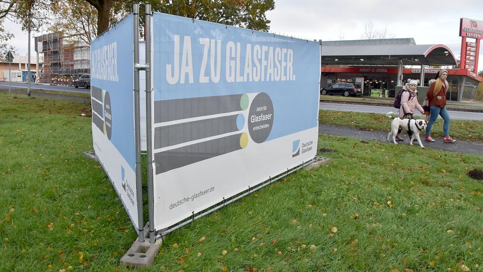Fußgängerinnen passieren großflächige Werbetransparente von Deutsche Glasfaser an der Rosenstraße in Marienhafe. Foto: Thomas Dirks
