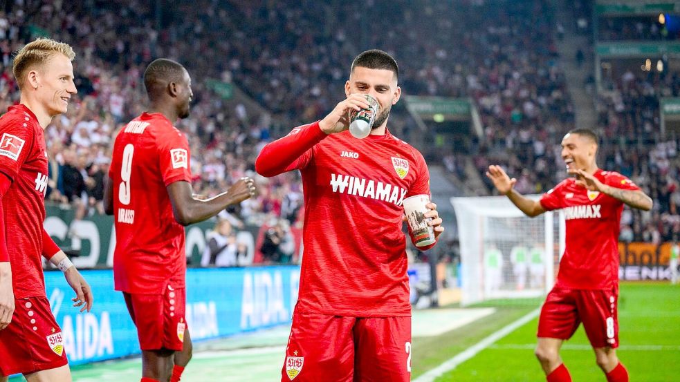 Deniz Undav (2.v.r.) feierte das 0:1 beim FC Augsburg mit einem Schluck Bier. Foto: Tom Weller/dpa