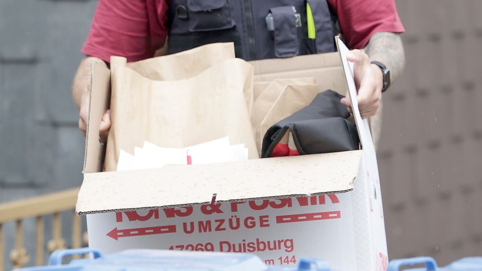 Ein Polizist trägt nach einer Wohnungsdurchsuchung einen Karton mit sichergestellten Gegenständen. Foto: David Young/dpa
