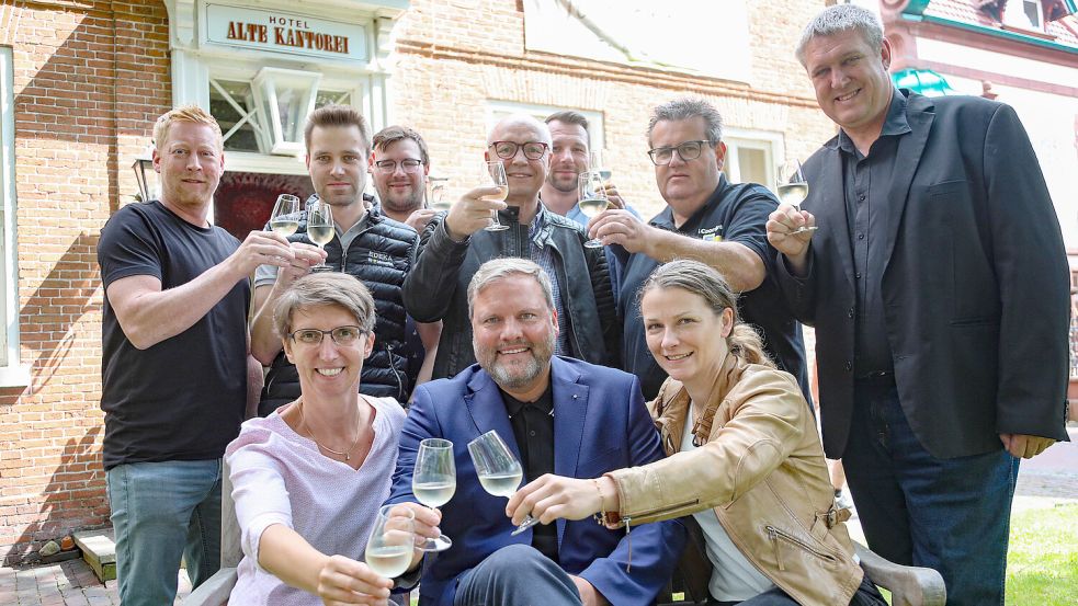 Mit einem Glas stoßen stehend von links Thomas Bruns (Edeka), Wilko Behrends (Edeka), Jan Pfeiffer (Hol’ ab!), Arnold Ackermann (Edeka), Sebastian Schmidt (Don A Roma), Jens Coordes (Edeka) und Jens Rohlfs (Hol’ ab!) sowie sitzend von links Sina Meisner (Weinschmecker), Udo Hippen (Kaufmännischer Verein) und Sandra Pfeiffer-Fecht (Stadt Aurich) auf das bevorstehende Wein- und Gourmetfest an. Foto: Romuald Banik