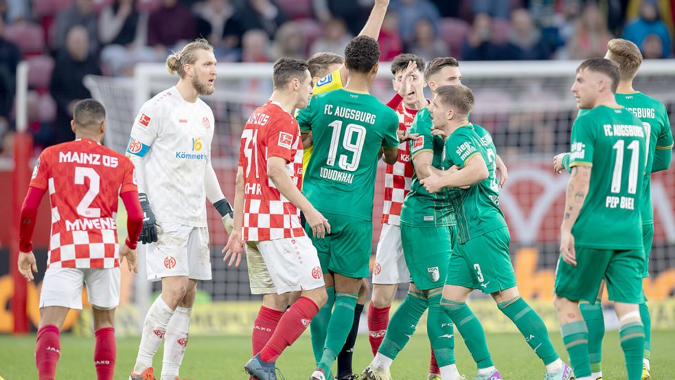 Die Spieler aus Mainz und Augsburg bilden ein Rudel, während Schiedsrichter Tobias Reichel die Rote Karte zeigt. Derartige Szenen sind seit der Fußball-Europameisterschaft nicht mehr möglich. Bis in die untersten Klassen darf nur noch der Kapitän mit dem Unparteiischen diskutieren. Foto: DPA