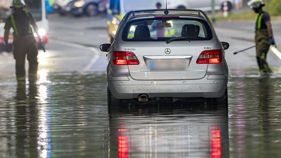 Ein Auto steckt am Montag in Duisburg im Hochwasser in einer Senke fest, während Feuerwehrleute die Gullydeckel öffnen, damit das Wasser nach einem Unwetter ablaufen kann. Foto: Christoph Reichwein/dpa