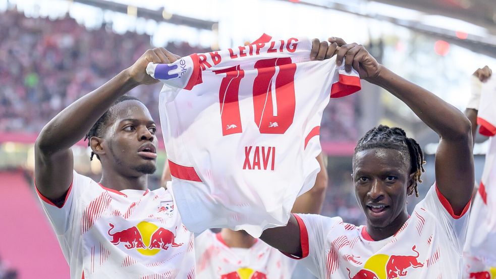 Leipzigs Castello Lukeba (l) und Amadou Haidara halten nach dem 2:1 ein Trikot des verletzten Xavi Simons nach oben. Foto: Hendrik Schmidt/dpa