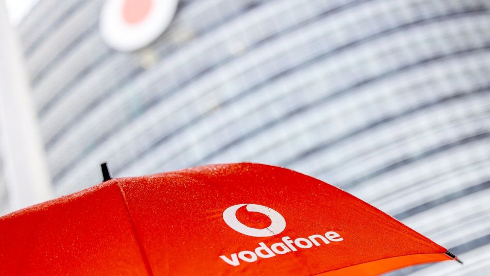 Ein Passant geht mit einem aufgespanntem Regenschirm mit dem Logo von Vodafone an der Zentrale der Deutschlandtochter des britischen Vodafone-Konzerns vorbei. Foto: Thomas Banneyer/dpa