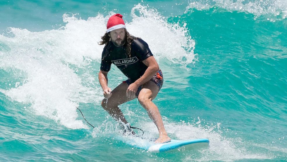 Surfende Santas gehören in Australien zu Weihnachten dazu. (Archivbild) Foto: Rick Rycroft/AP/dpa