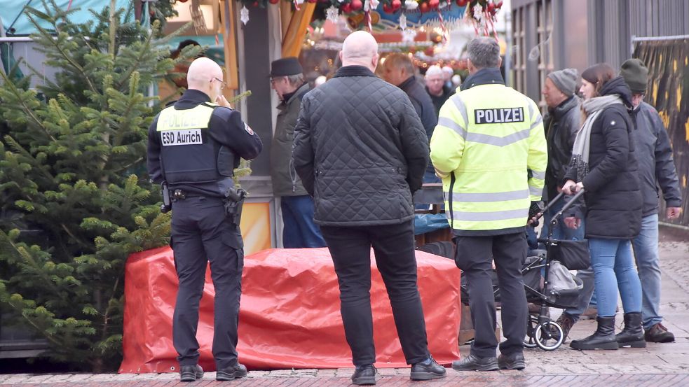 Vertreter von Polizei und Stadt Aurich sehen sich am Sonnabend einen mit Plane kaschierten Betonblock am Eingang zum Auricher Weihnachtsmarkt an. Foto: Thomas Dirks