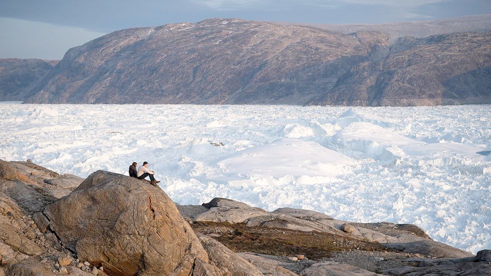 Zwei Studenten der New York University sitzen auf einem Felsen mit Blick auf den grönländischen Helheim-Gletscher. Foto: Felipe Dana/AP/dpa