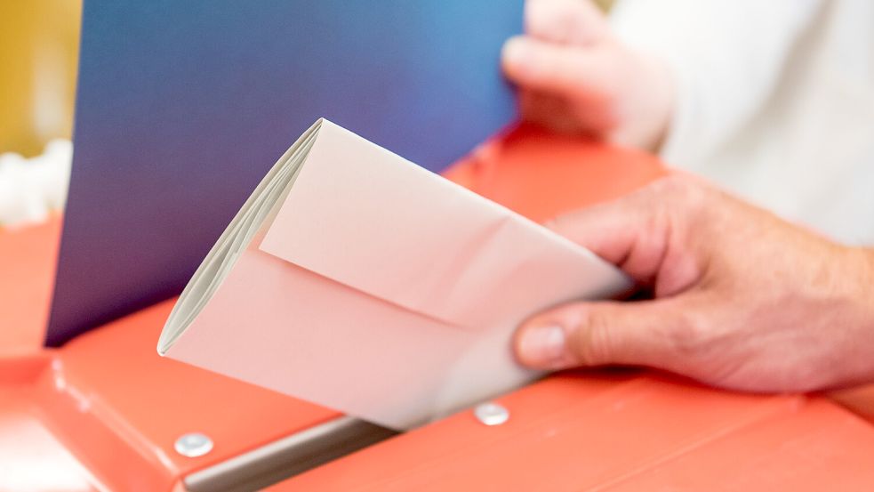 Ein Wahlhelfer steckt in einem Wahllokal den Stimmzettel eines Wählers in eine Wahlurne. In Großefehn haben sich bereits besonders viele Freiwillige für diese Aufgabe gemeldet. Foto: Daniel Bockwoldt/DPA