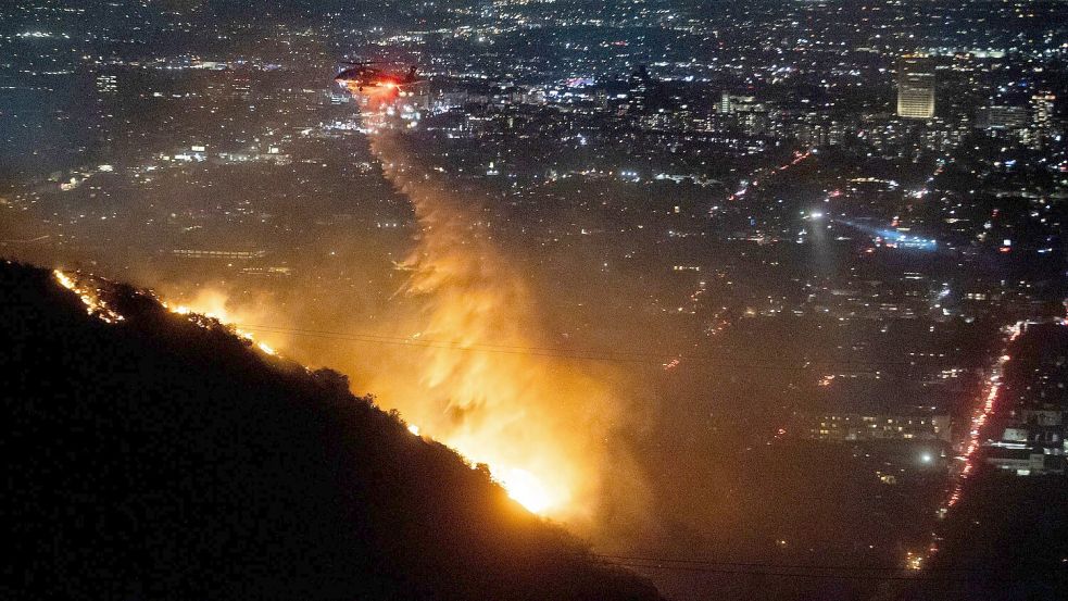 Ein Hubschrauber wirft Wasser auf das brennende Sunset Fire in den Hollywood Hills. Foto: Ethan Swope/AP/dpa